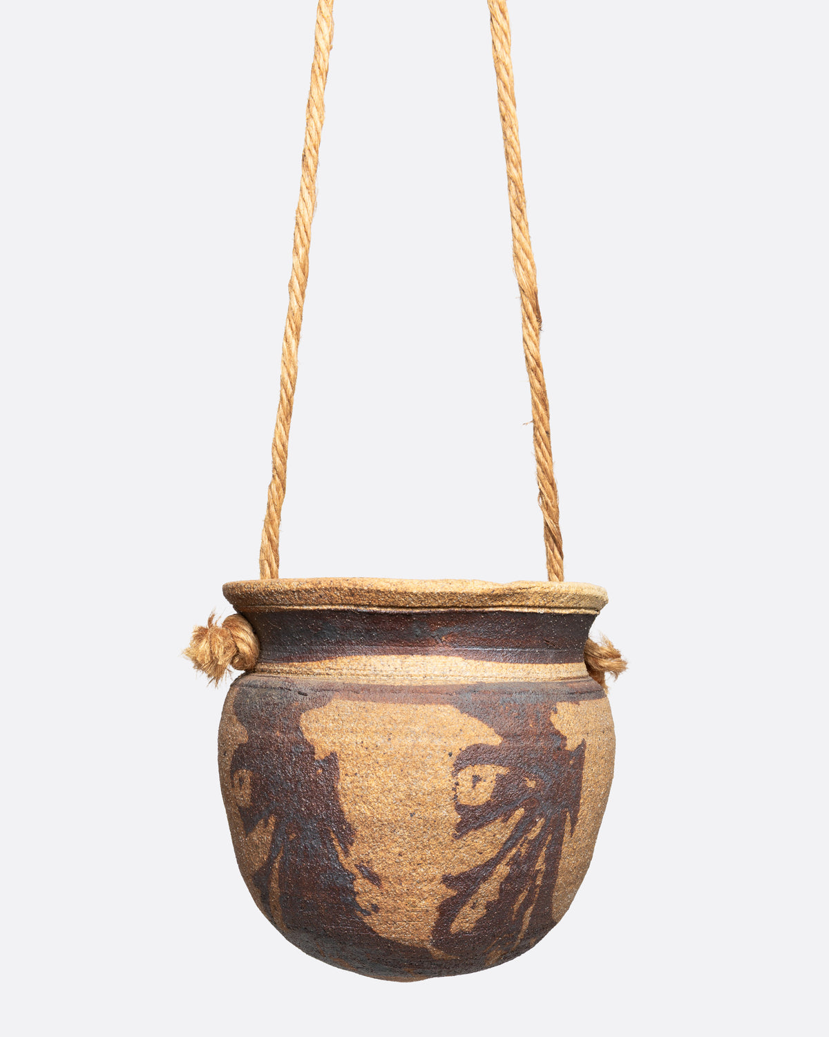 A ceramic pot with an abstract tan and brown pattern and cords for hanging, shown from the front.