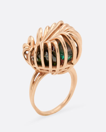 Sara Katherine Jacobson Rattled Distorted ring in rose gold, swirling gold wires forming a cage around a loose emerald and tourmalines