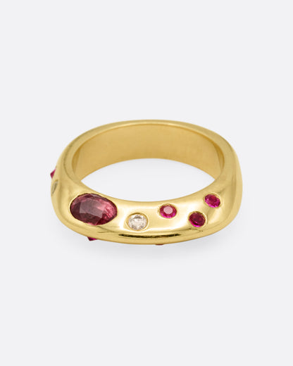 Yellow gold band with scattered rubies and diamonds, angled view with the oval ruby facing left