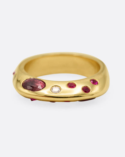 Yellow gold band with scattered rubies and diamonds, front view of the band with an oval ruby among smaller rubies and diamonds