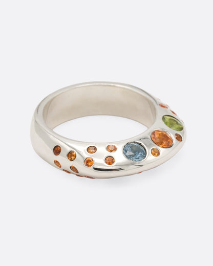 A dimensional sterling silver ring with orange, blue, and pink sapphires on either side, shown from the side.