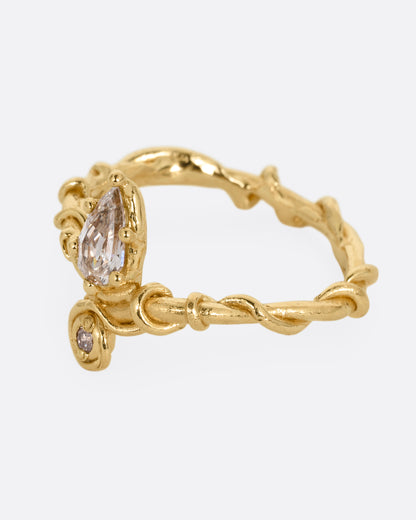 A yellow gold ring with a vine wrapped band and two stacked diamonds, one pear one round. Shown from the side.