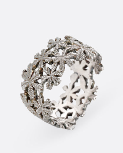 A wide silver ring with a pattern of flowers, shown standing up from the front.
