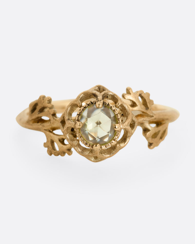 A yellow gold ring with a floral motif and peridot. Shown from the front.