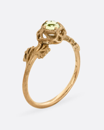 A yellow gold ring with a floral motif and peridot. Shown standing up from the side.