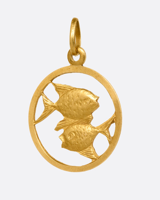 A circular yellow gold pendant with two fish and on open center with cutouts. Shown from the front.