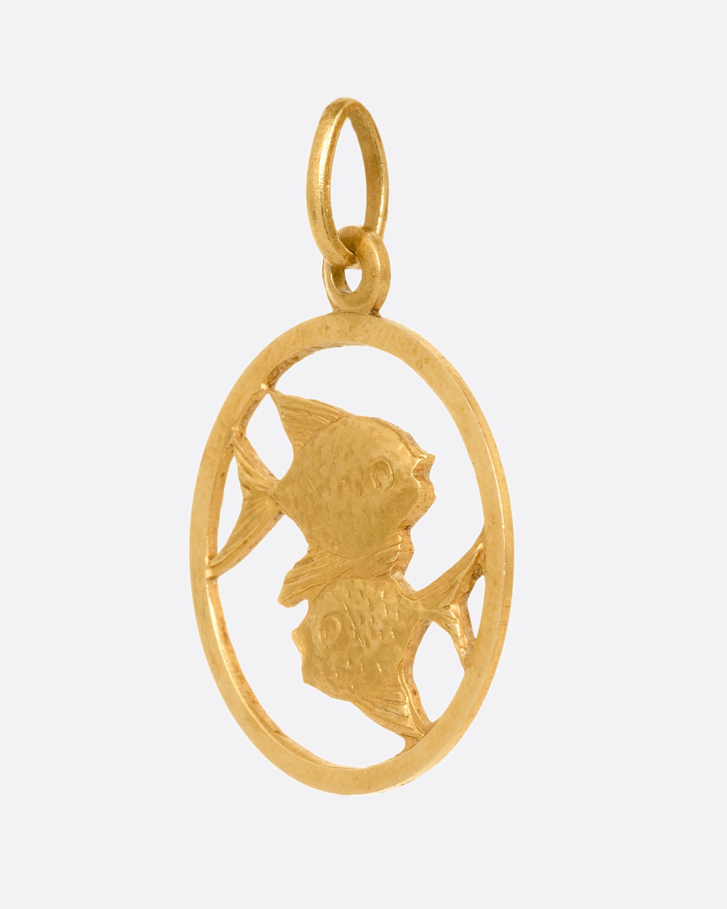 A circular yellow gold pendant with two fish and on open center with cutouts. Shown from the side.