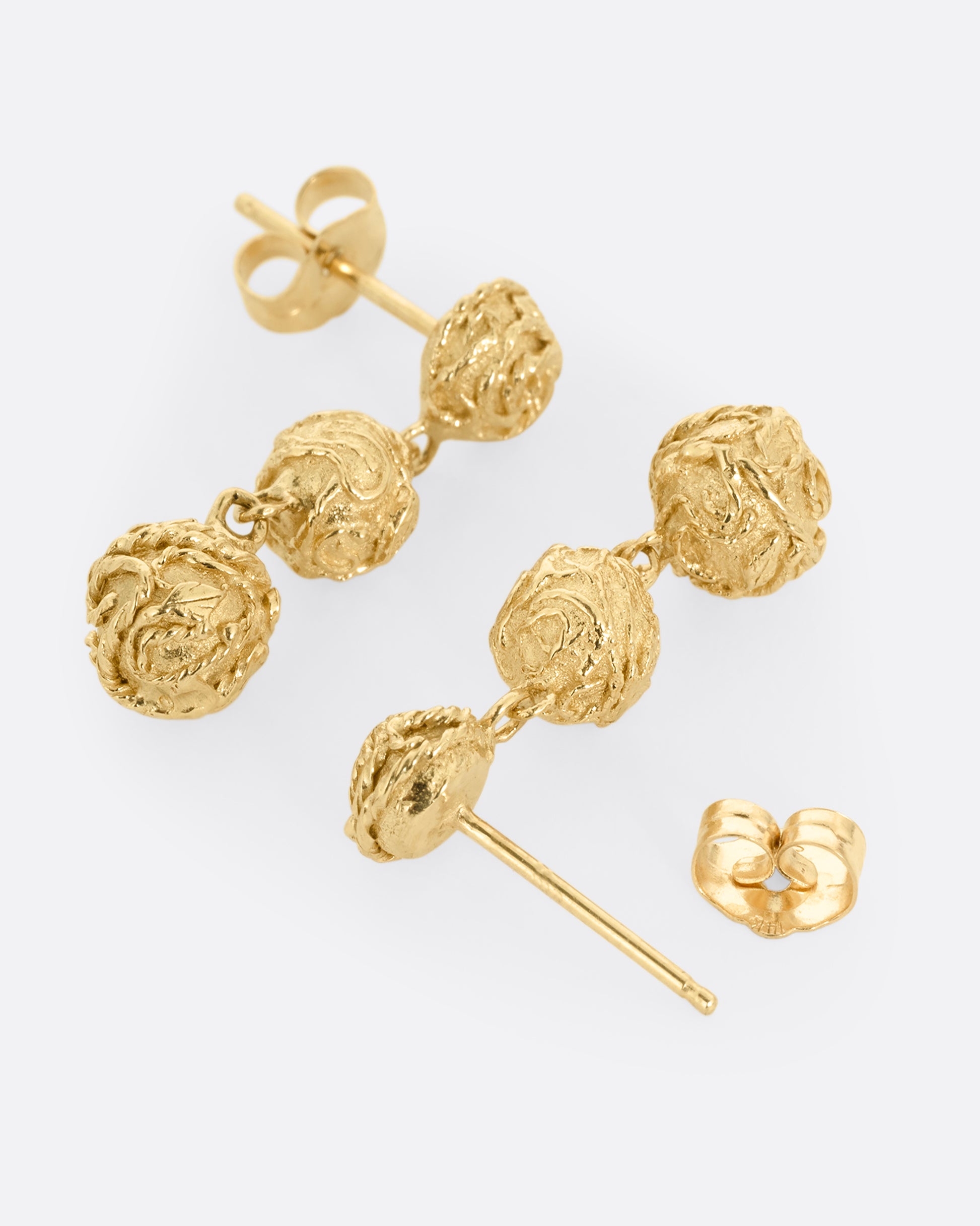 A pair of yellow gold dangle earrings with three linked spheres. Shown lying flat from the side. One earring its facing front, the other is open facing back.