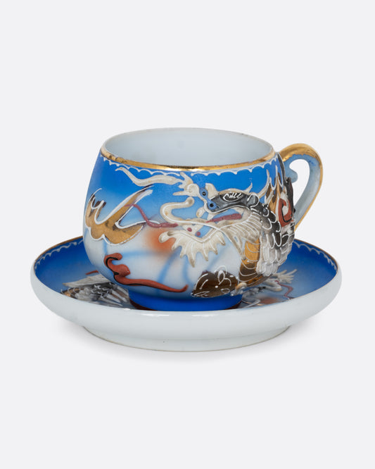 A dragonware moriage teacup and saucer with an enamel dragon motif in vibrant hues. A lithophane nude figure sits at the base of the cup. Shown from the side.