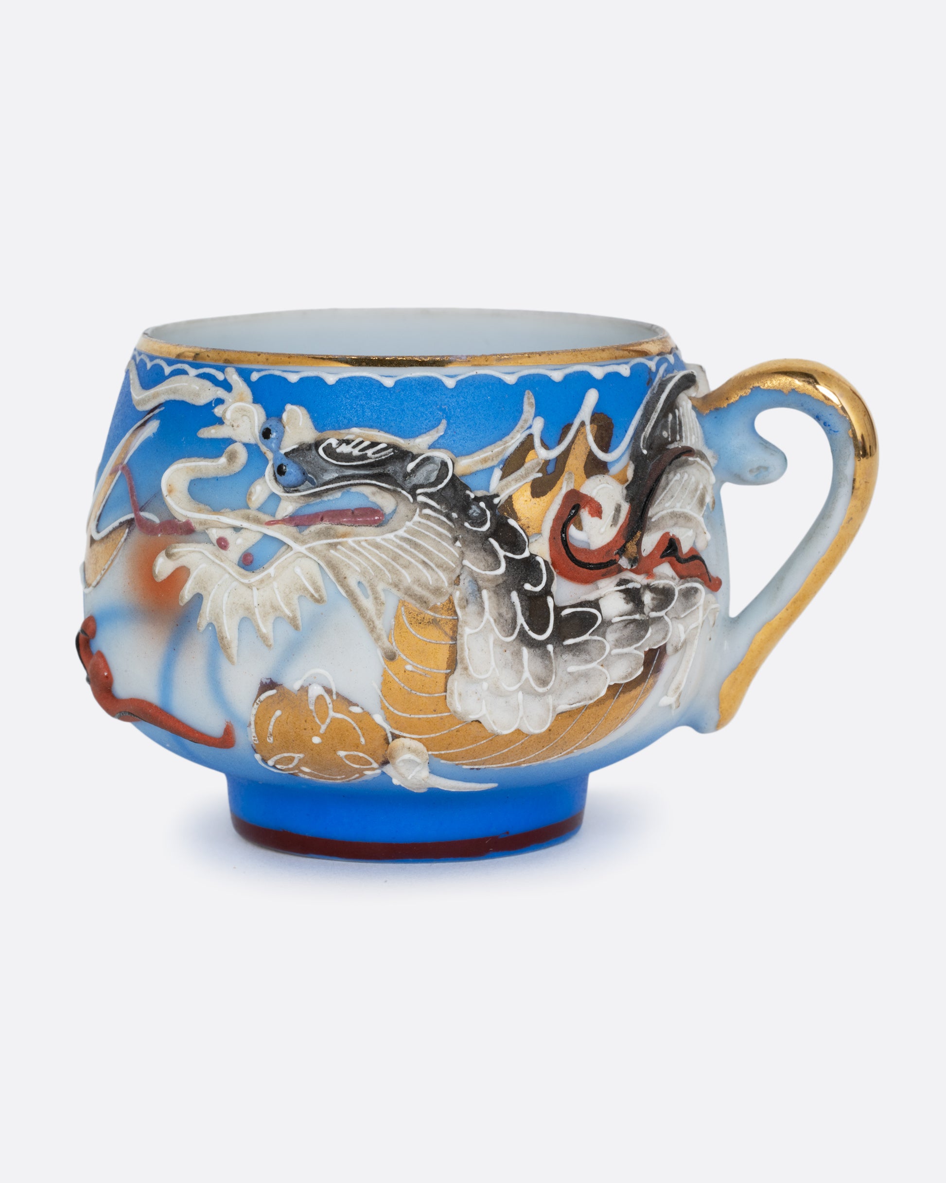 A dragonware moriage teacup with an enamel dragon motif in vibrant hues. A lithophane nude figure sits at the base of the cup. Shown from the side.