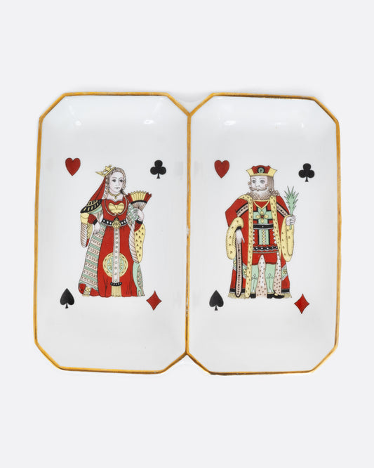 A white dish with gold trim and two playing cards, one a King and the other the Queen. Each has the four card suits on each corner. Shown from the top.