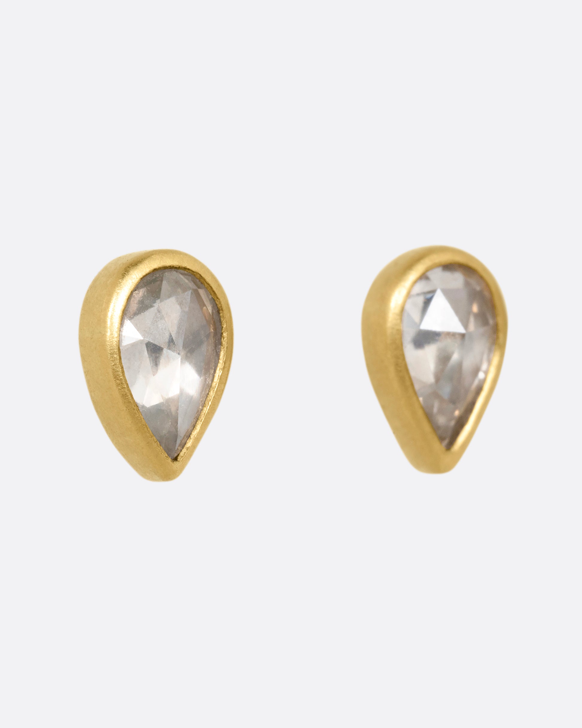 A pair of yellow gold tear drop shaped stud earrings with diamonds. Shown from the side.