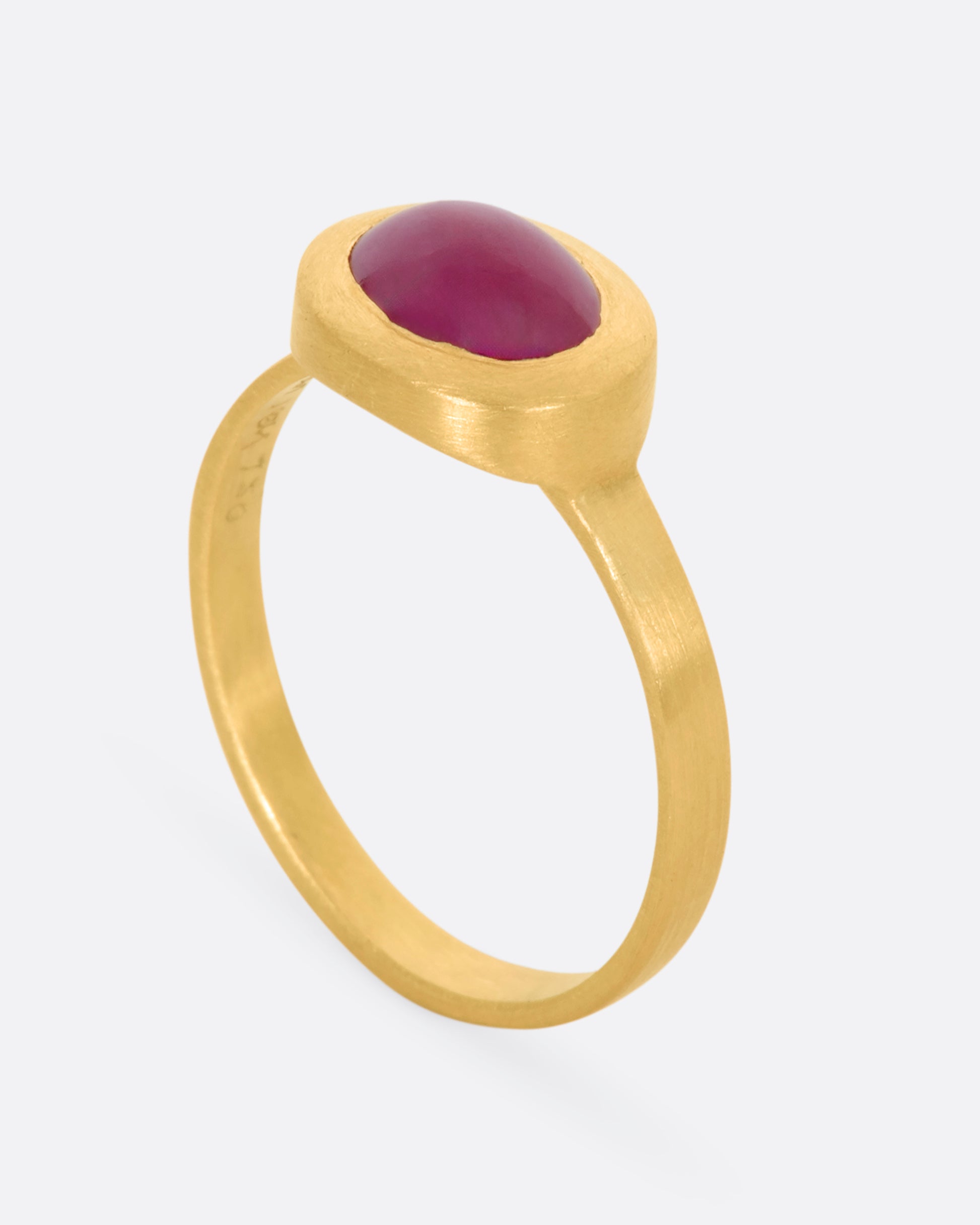 A yellow gold ring with a ruby cabochon. View from the side, standing up.