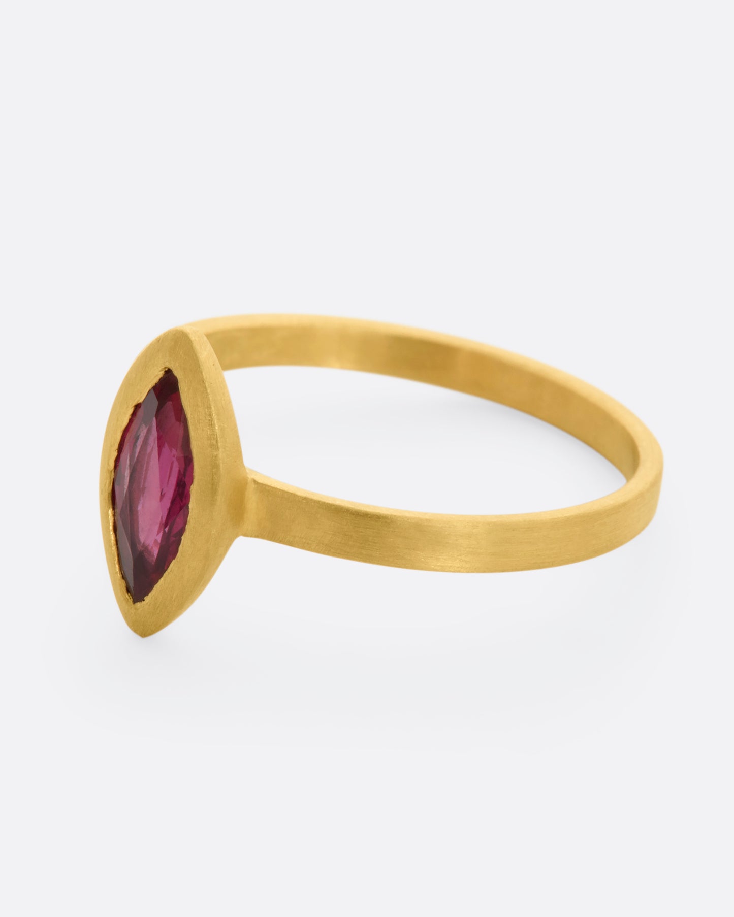 A matte yellow gold ring with a bezel set ruby marquise. View from the side.