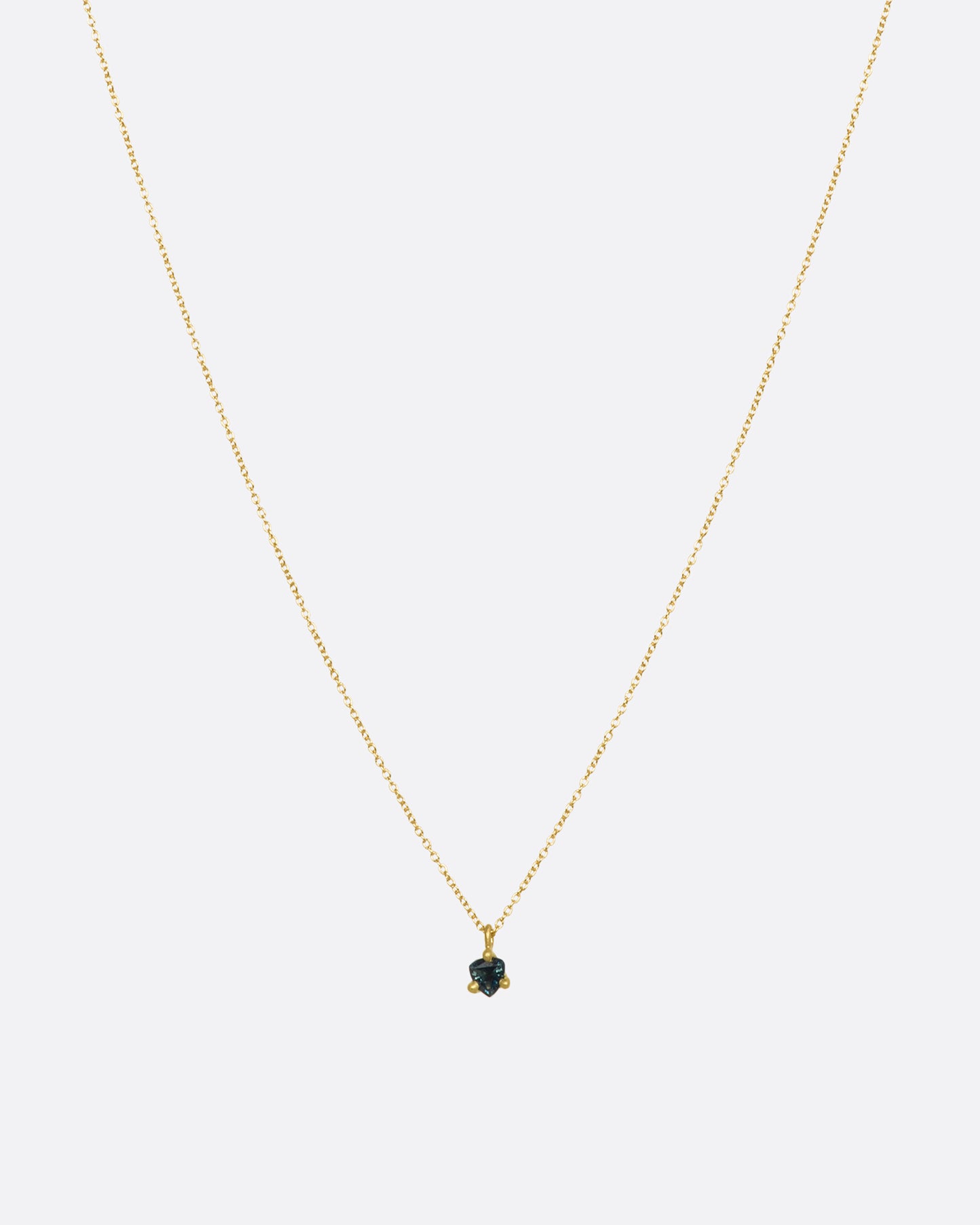 A matte yellow gold prong set triangle teal sapphire necklace. View from the front.