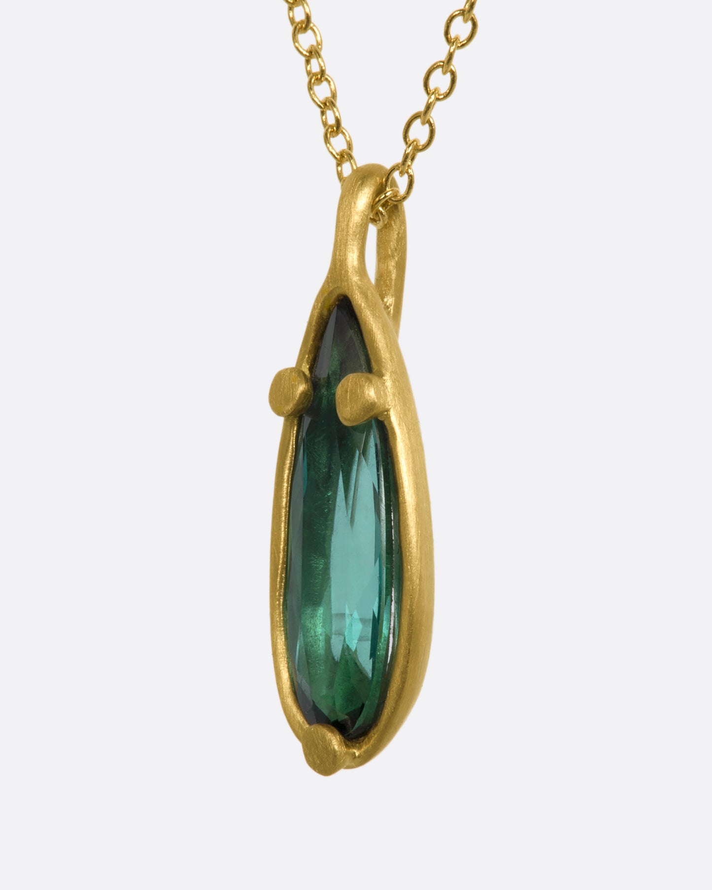 A matte yellow gold necklace with a large pear shaped teal tourmaline pendant. View from the side.