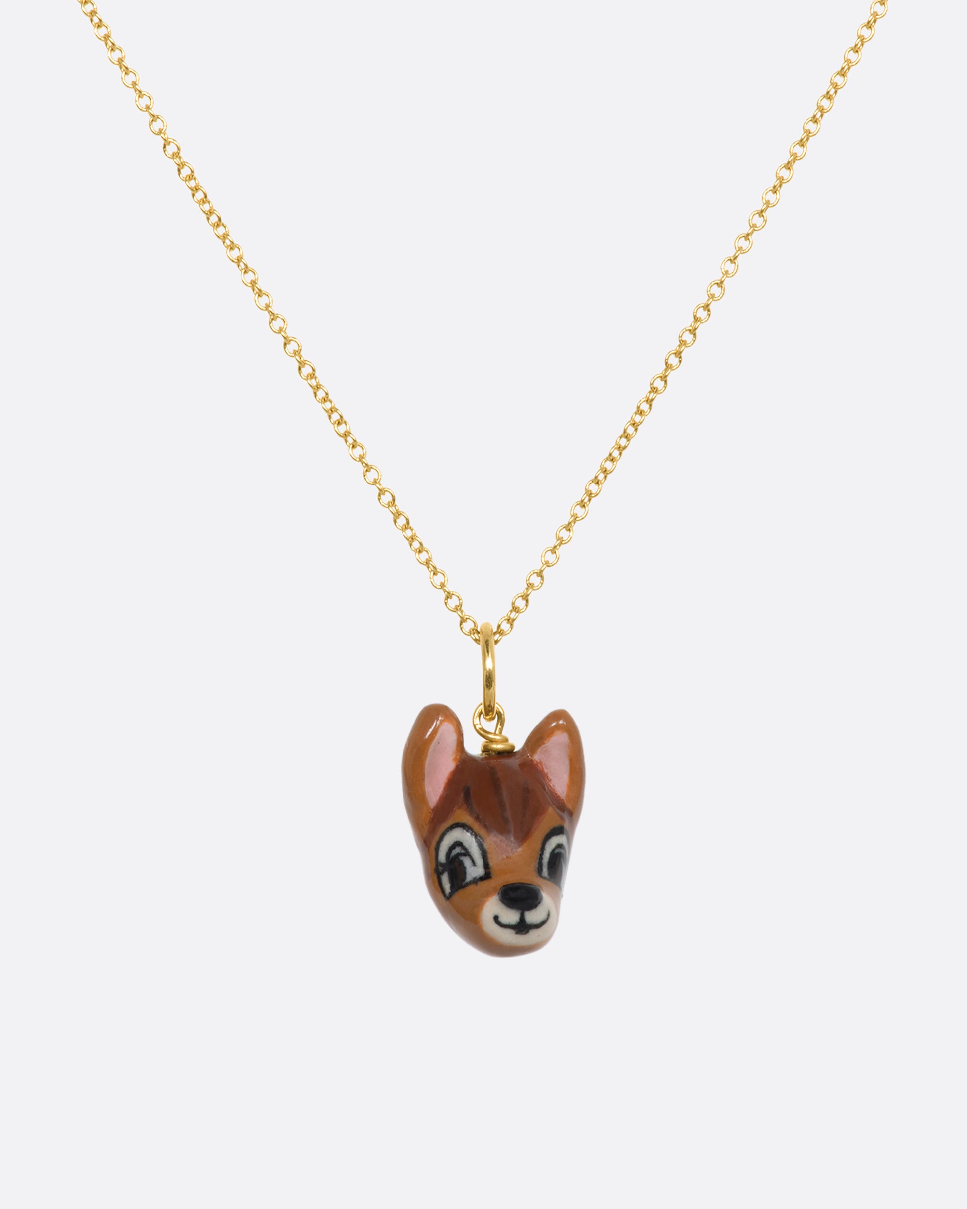 A hand painted 3D porcelain Bambi charm with a yellow gold bail. Shown on a chain.