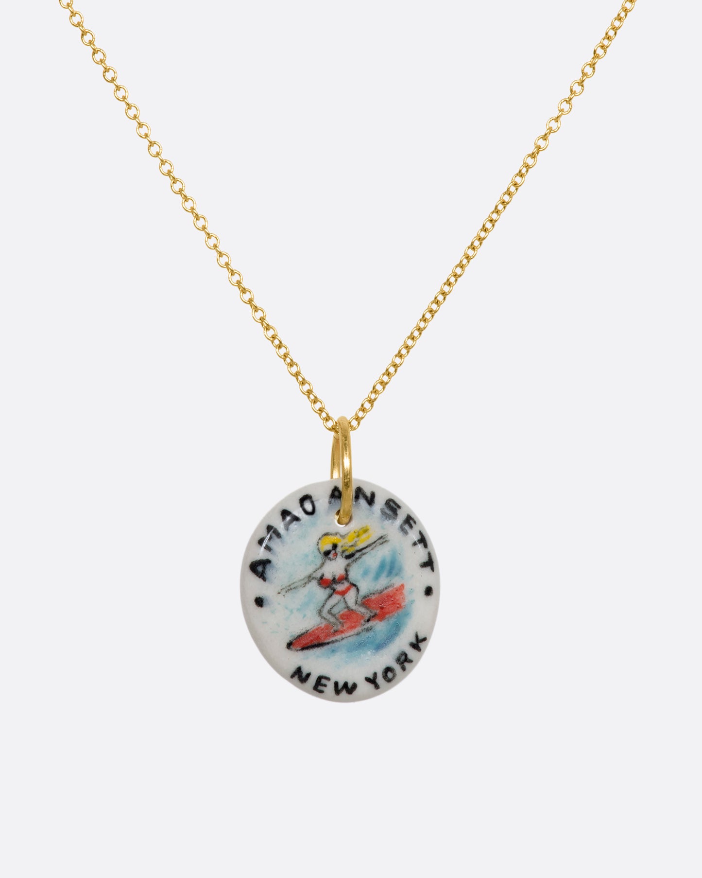 A hand painted porcelain charm with a blond woman in a bikini surfing on it and the words "Amagansett New York". View on a chain.