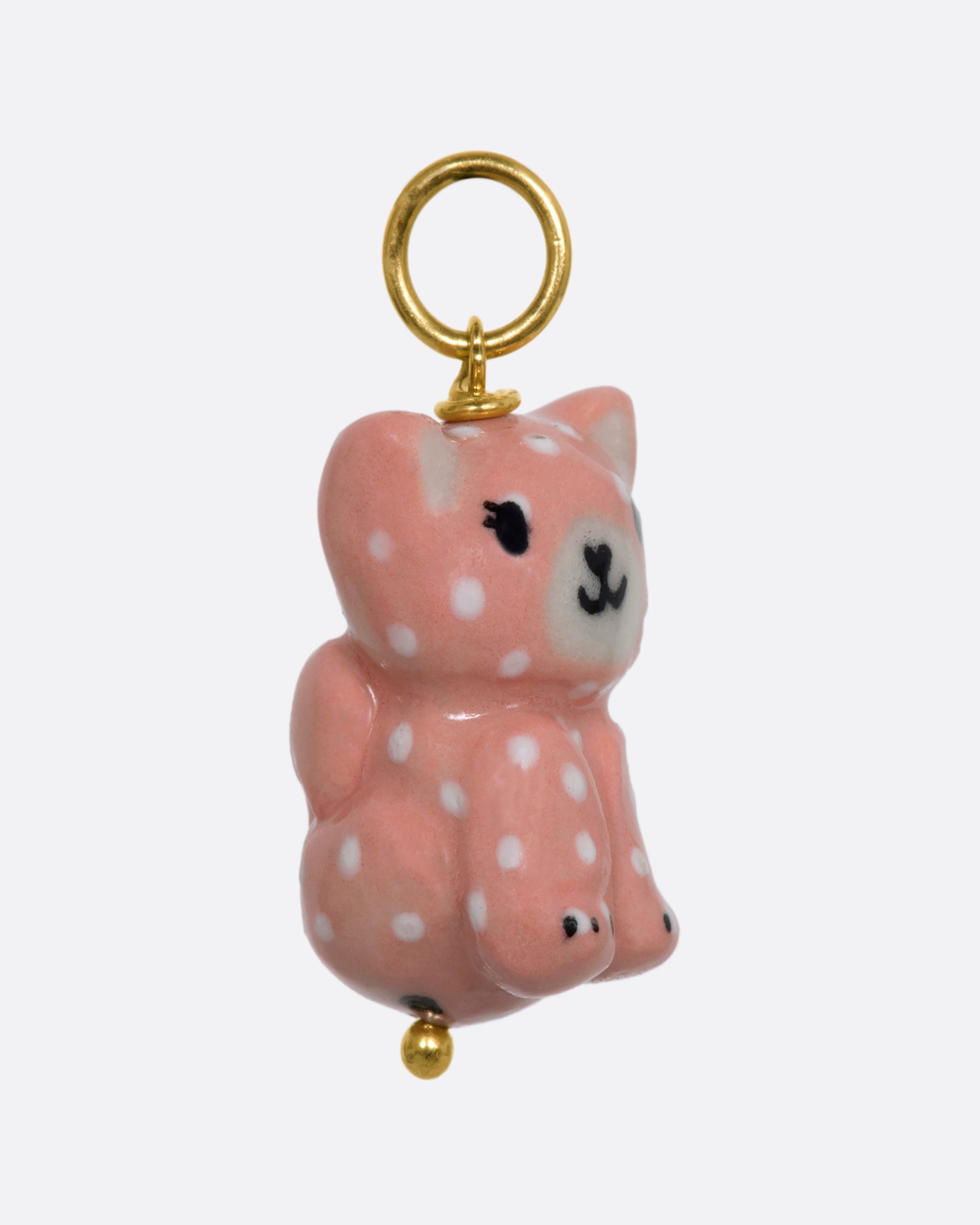 A three dimensional porcelain pink cat charm with white spots. View from the side.