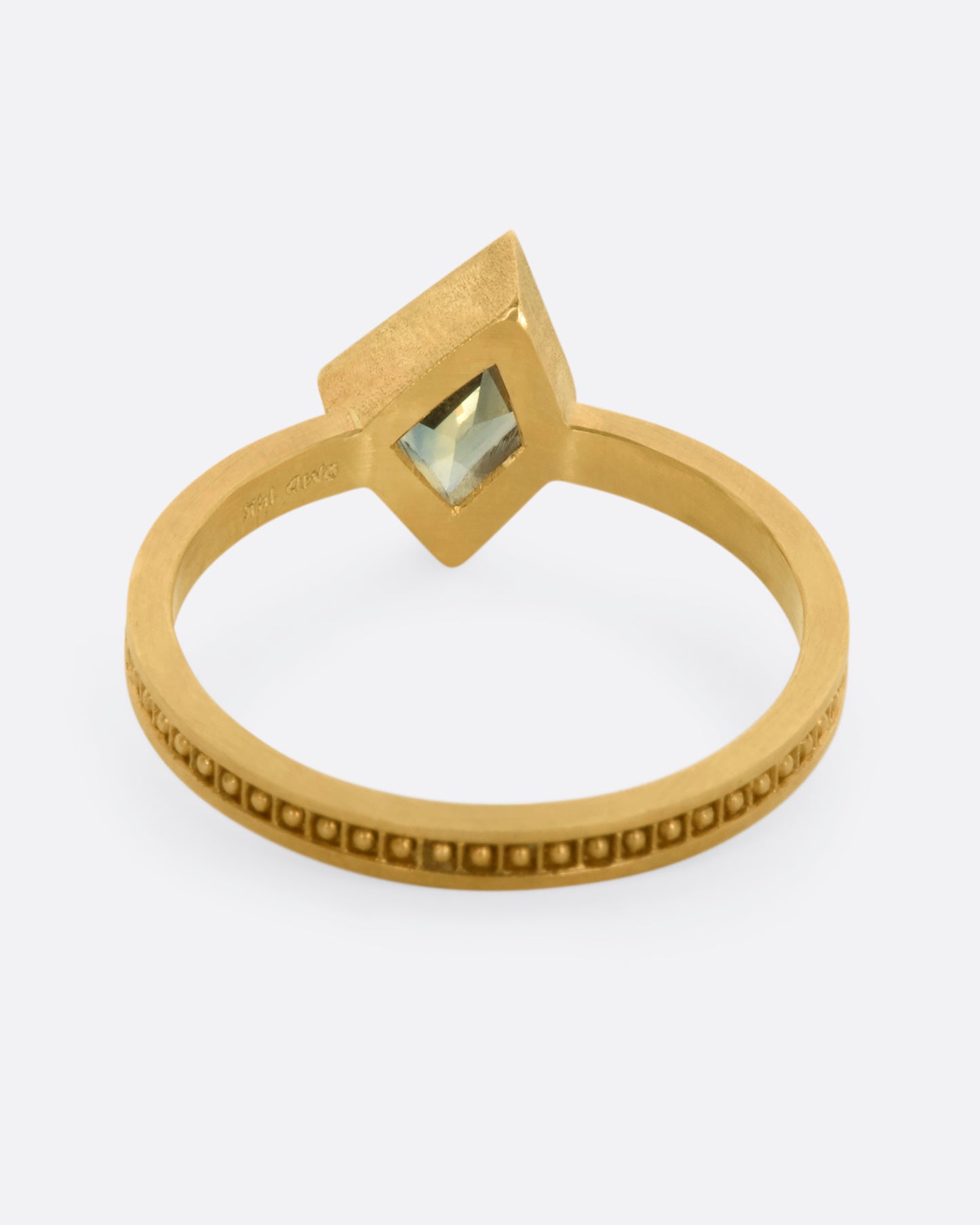 A yellow gold ring with a trapezoid green sapphire and raised dots in square shaped holes around the band. View from the back.