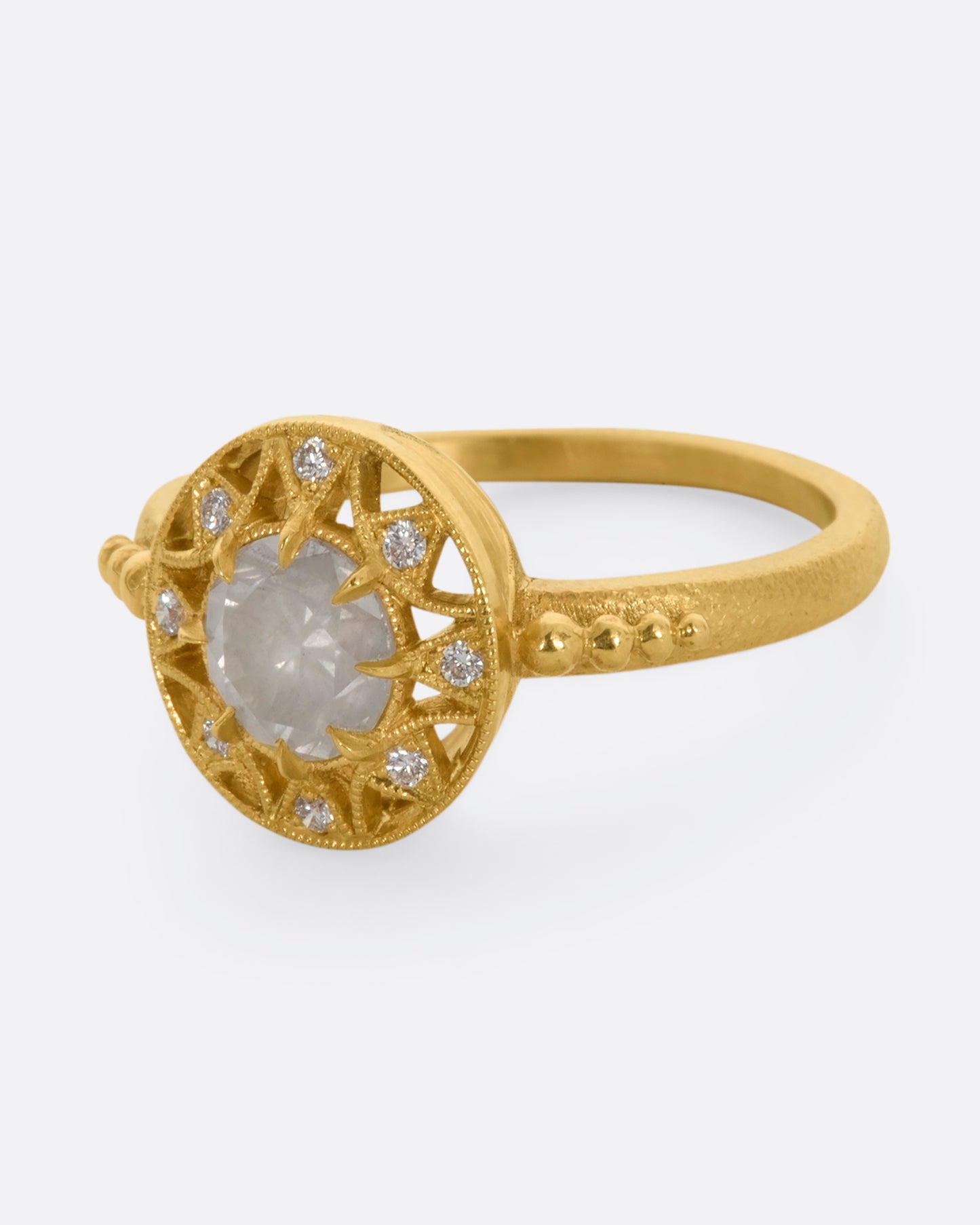 A yellow gold ring with a rose cut opalescent diamond at the center and a ring of brilliant cut diamonds around the face. View from the side.