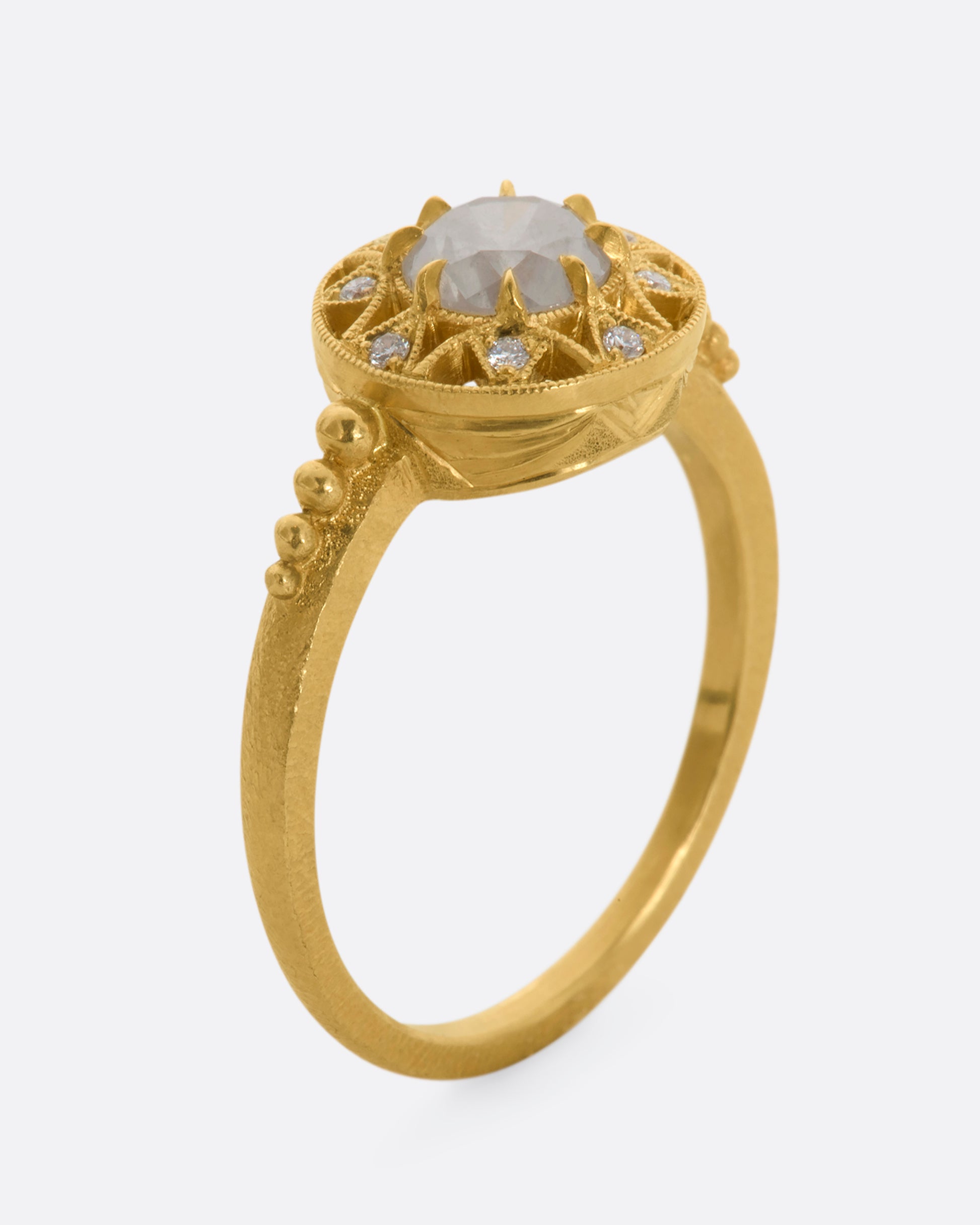 A yellow gold ring with a rose cut opalescent diamond at the center and a ring of brilliant cut diamonds around the face. View standing up.