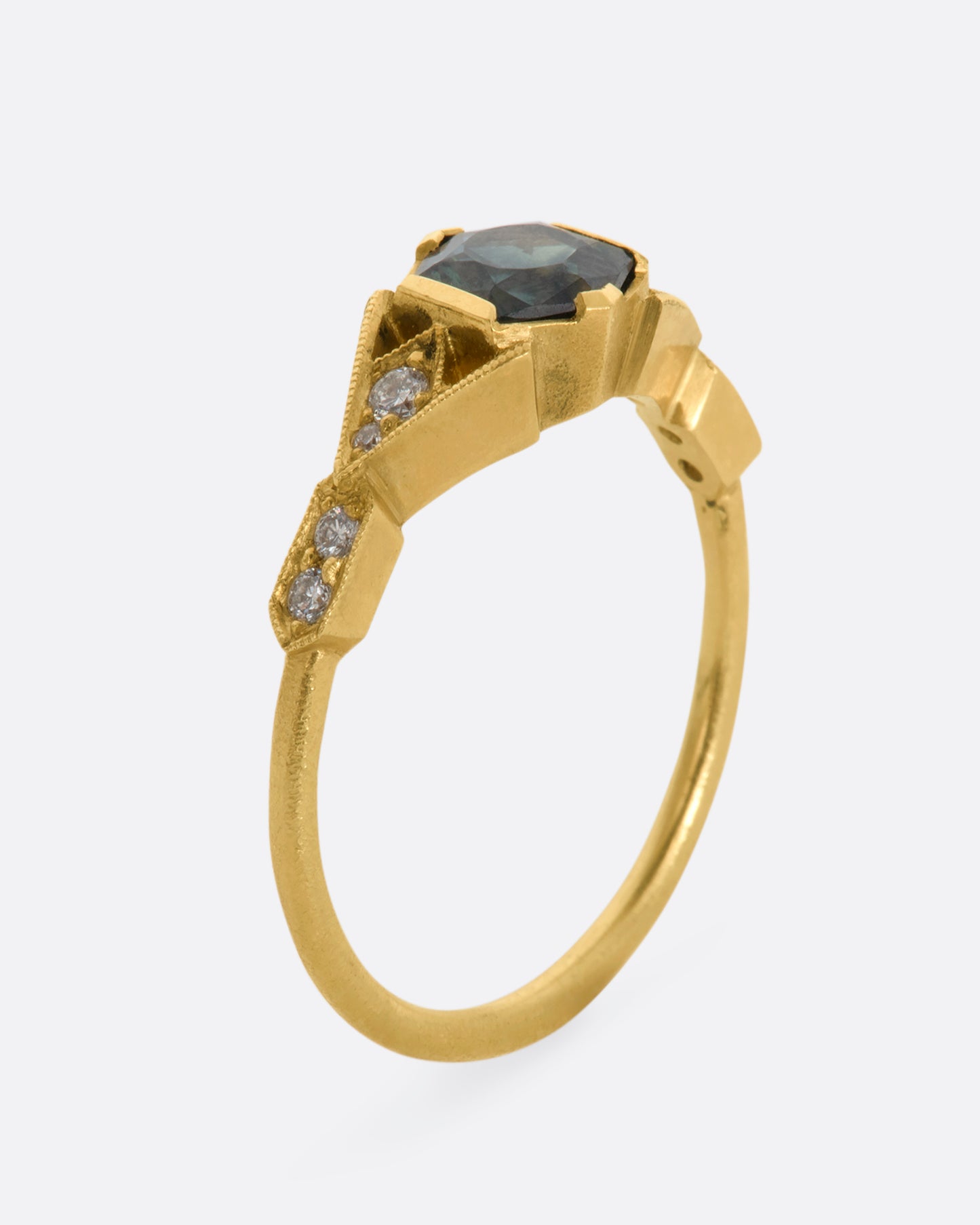 A yellow gold ring with deep teal sapphire and diamonds. View standing up.