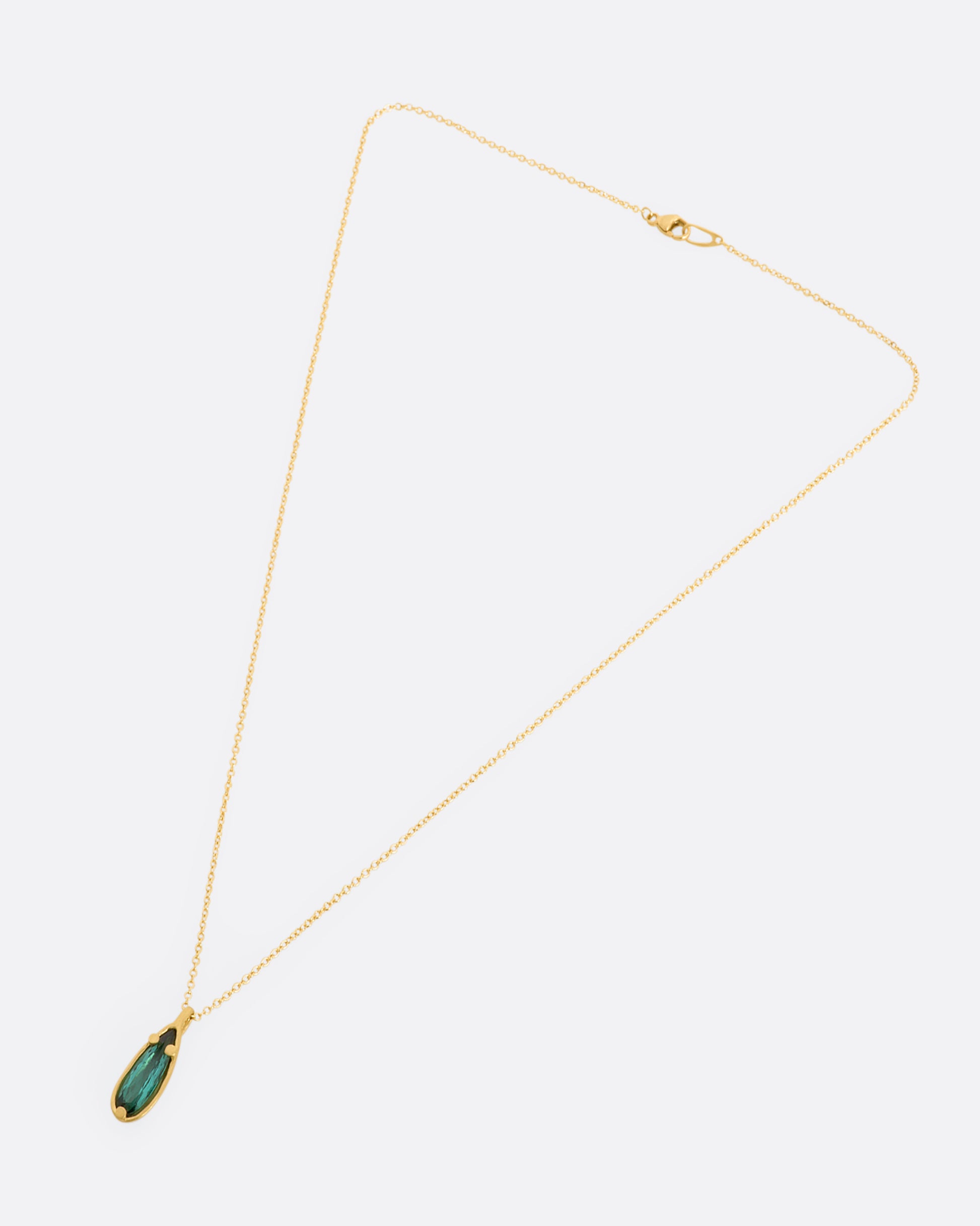 A matte yellow gold necklace with a large pear shaped teal tourmaline pendant. View laying flat.