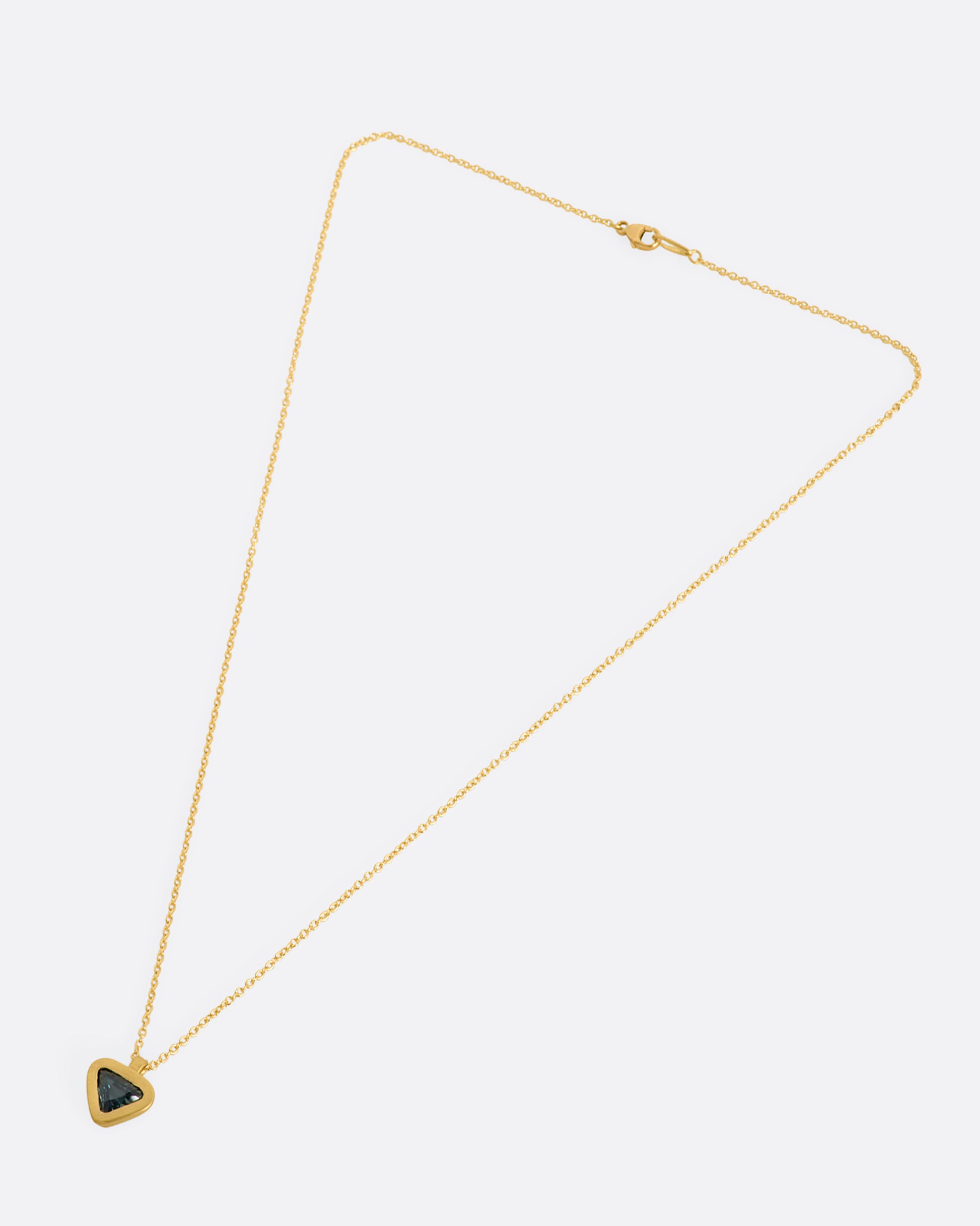 A yellow gold pendant with a triangle green sapphire pendant. View laying flat.