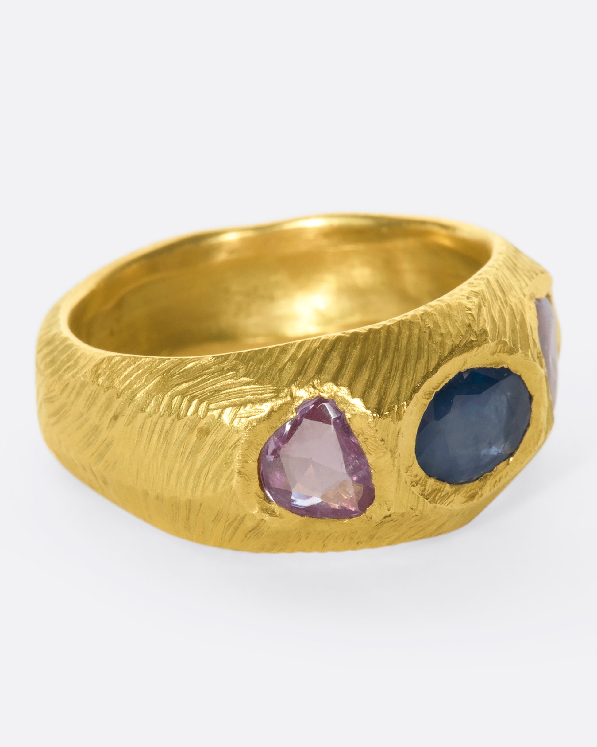 This hand carved 18k gold band is inlaid with an oval blue sapphire, flanked by beautiful pink sapphires