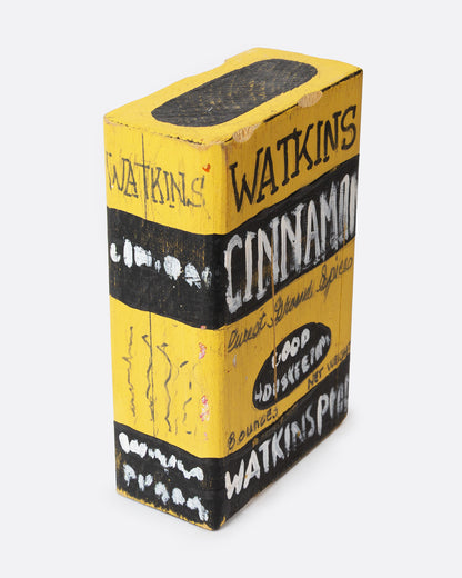 A yellow and black hand painted wooden box with the text 'WATKIN'S CINNAMON', shown from the side.