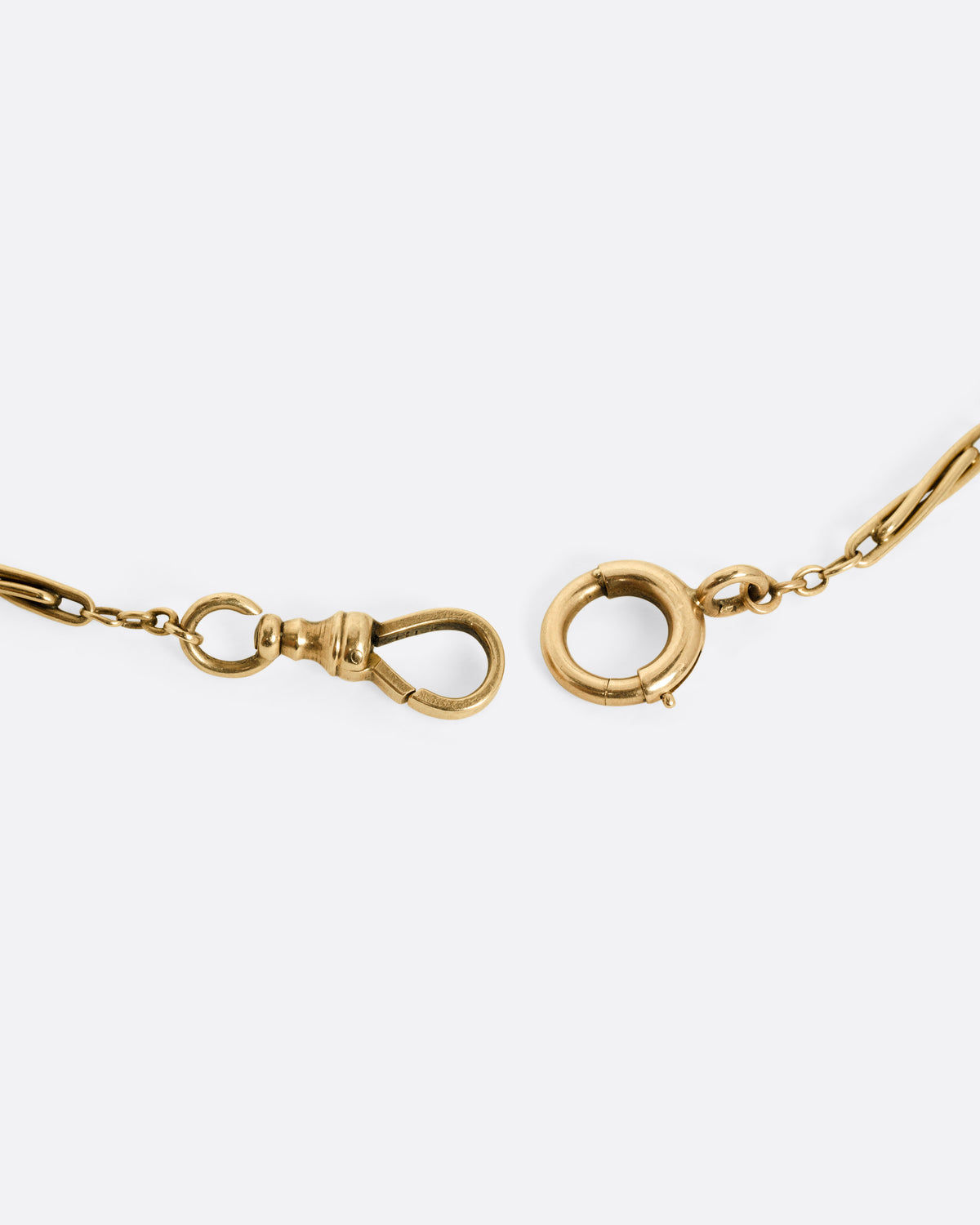 A close up of a yellow gold clasp on a Victorian watch chain necklace.