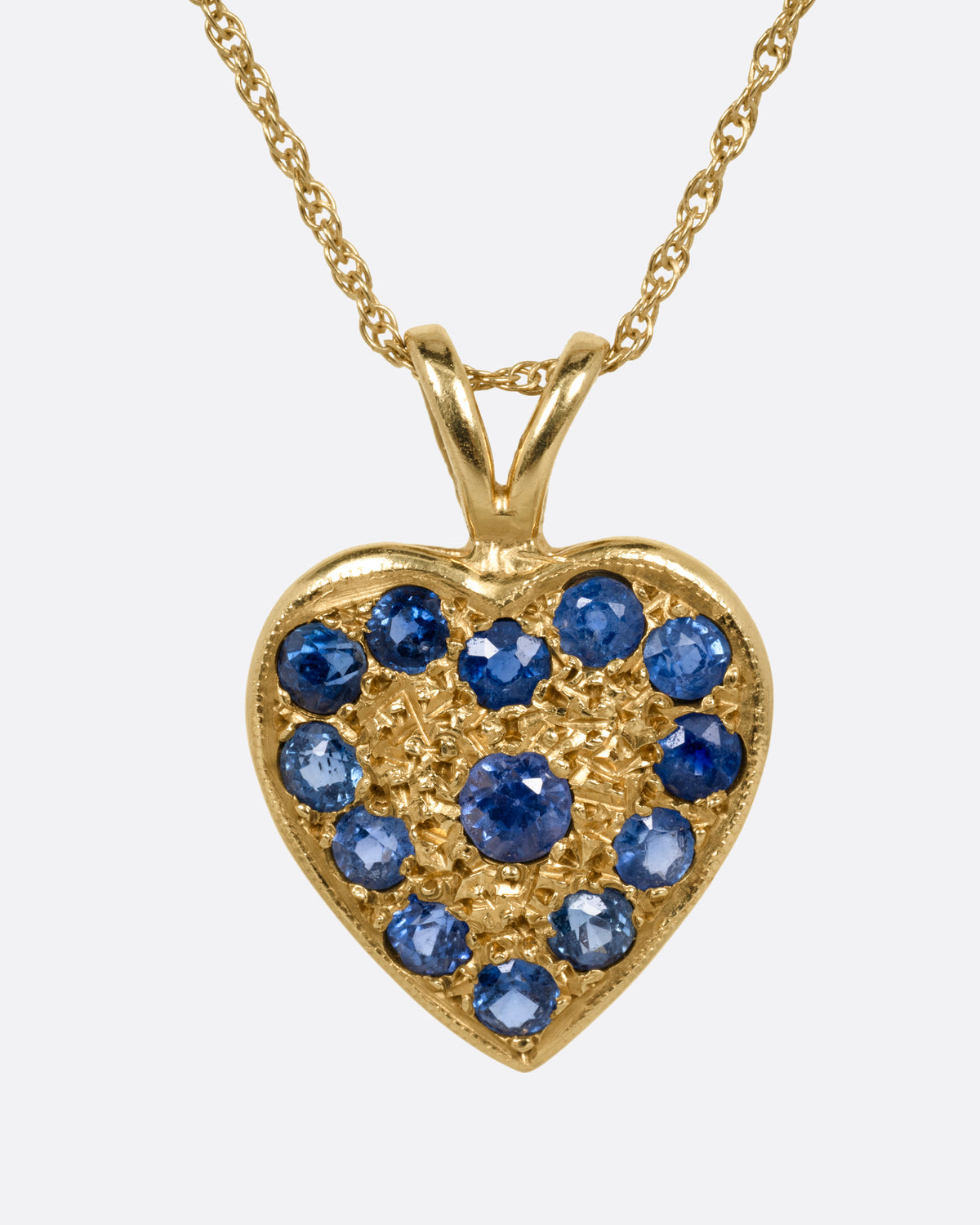 A yellow gold necklace with a heart shaped pendant with blue sapphires, shown from the front.