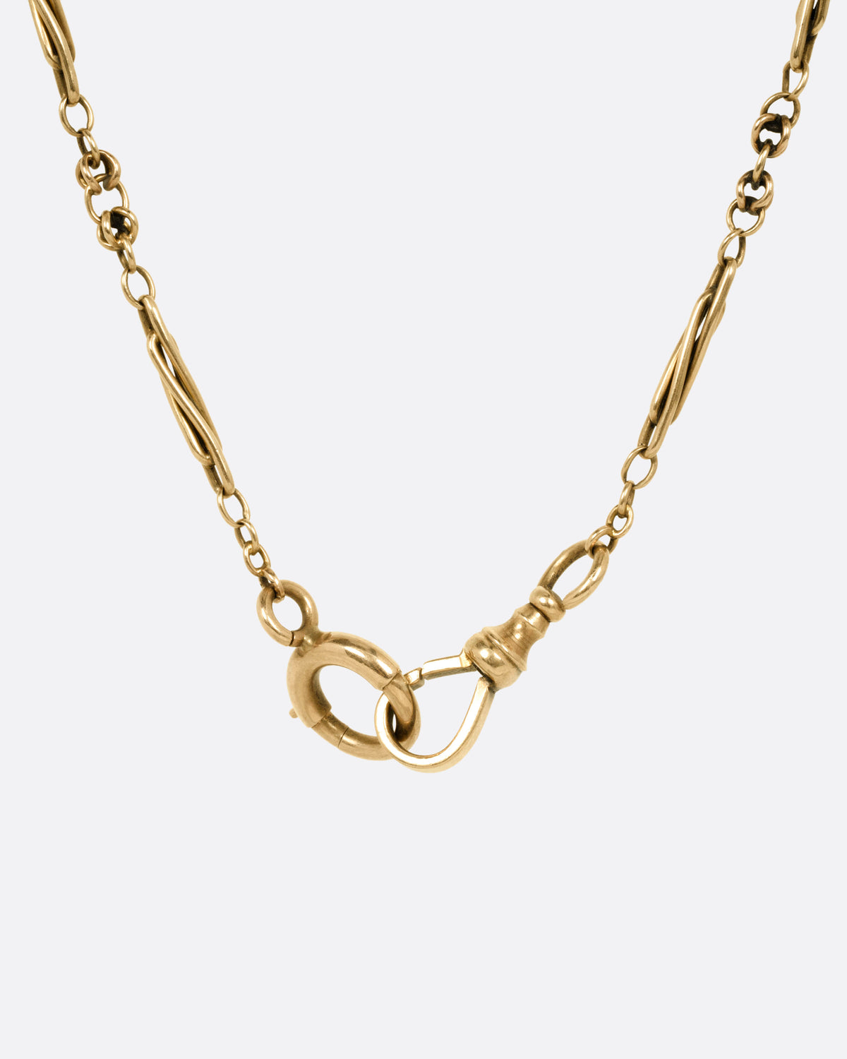 A close up of a yellow gold clasp on a Victorian watch chain necklace.