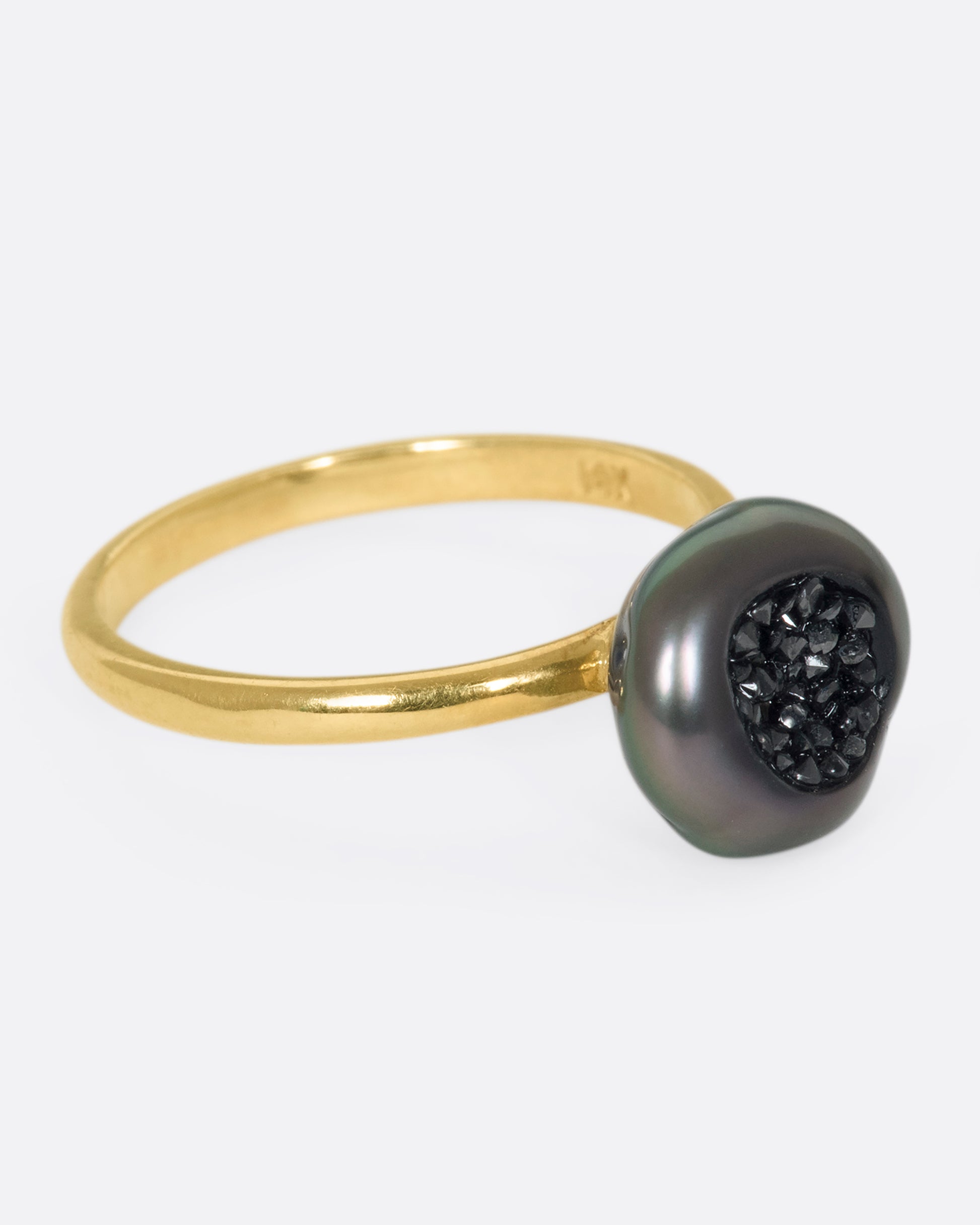 A 14k gold band with a carved Tahitian keshi pearl lined with black diamonds