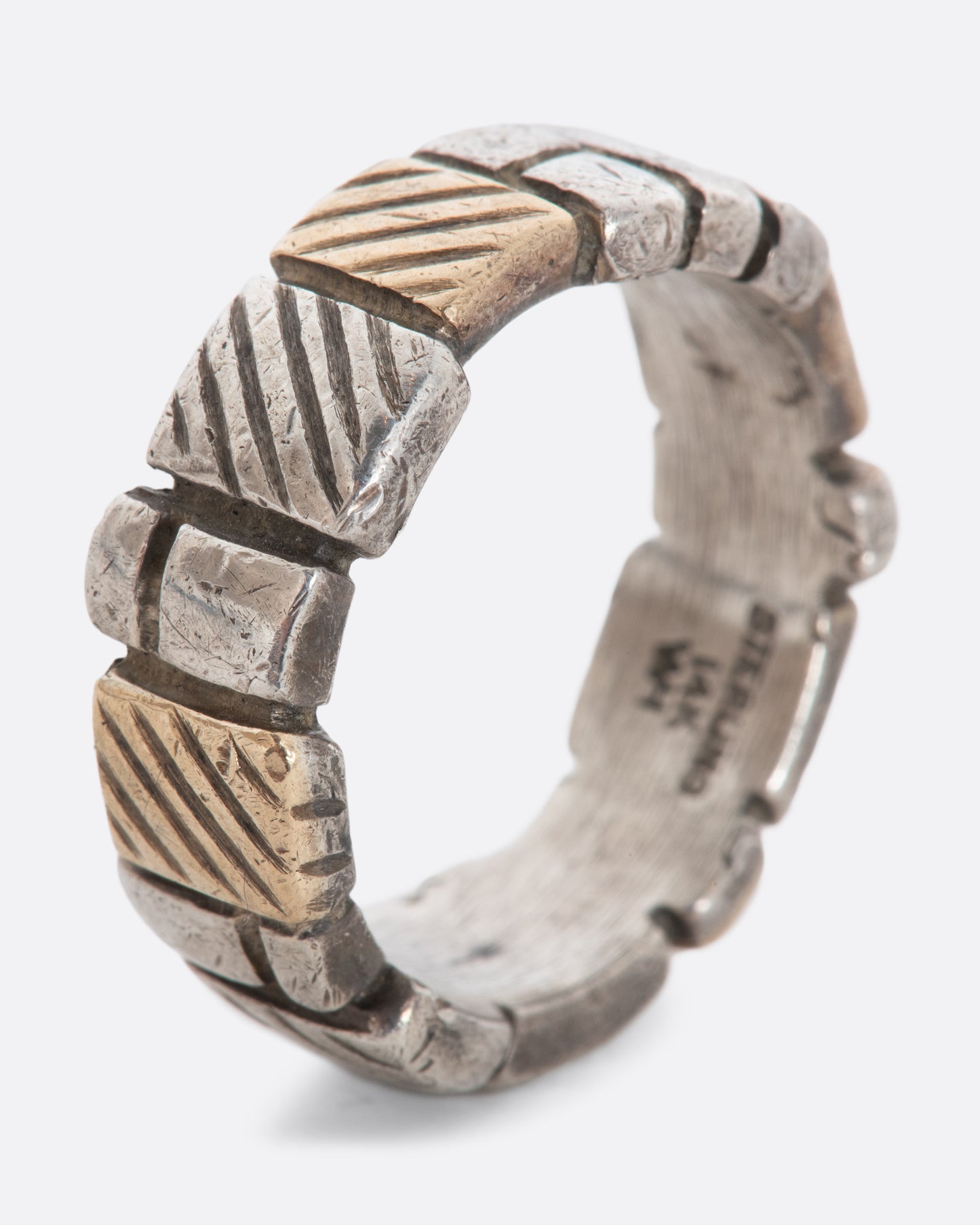 A textured sterling silver and yellow gold band with squares all around. View from the side, standing. 