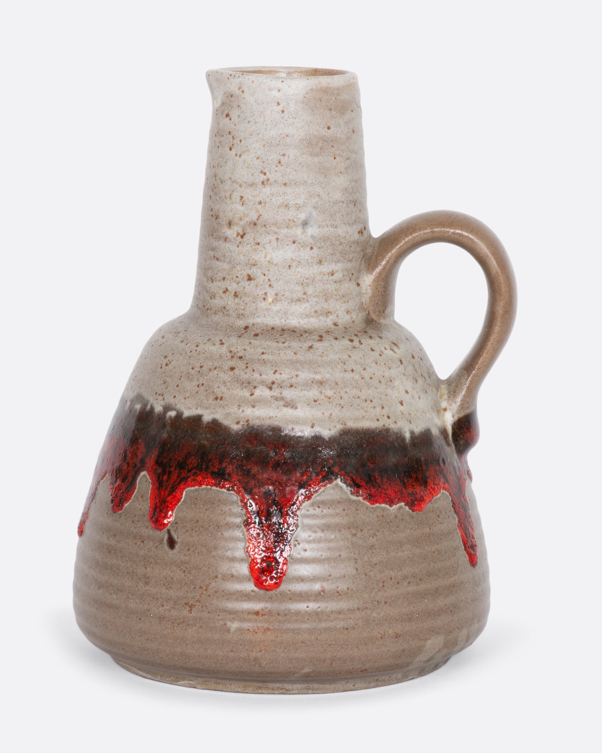 A greige ceramic pitcher with red dripping glaze. View from the side.