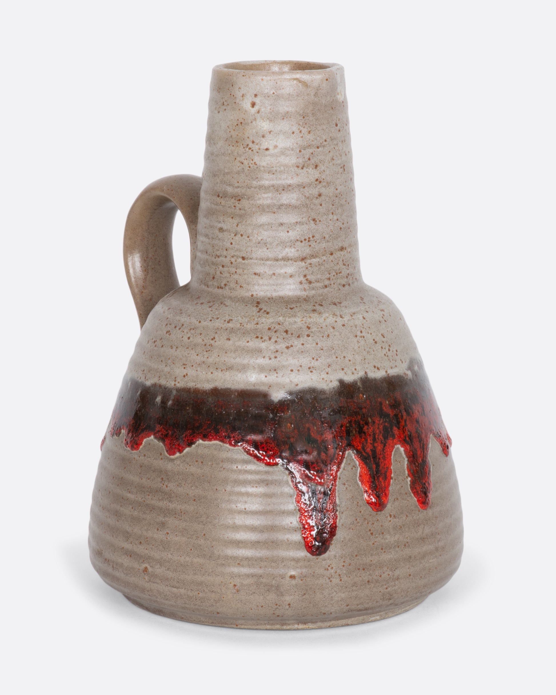 A greige ceramic pitcher with red dripping glaze. View from the alternate side.