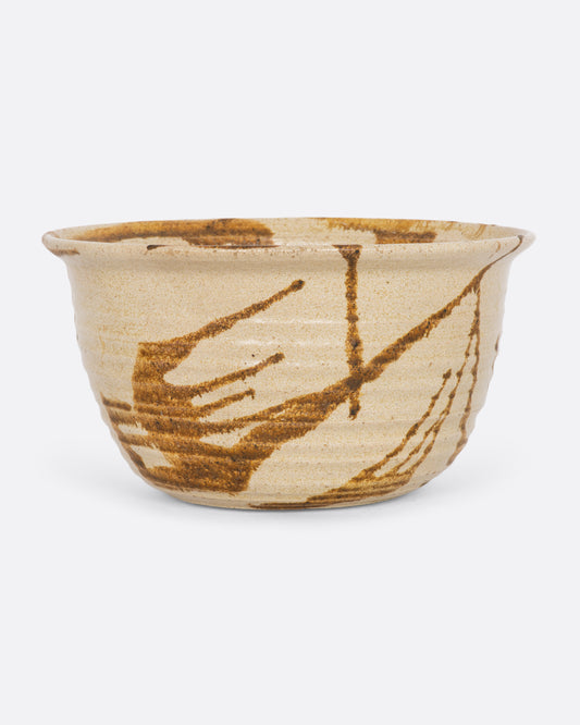 A beige ceramic bowl with brown splatter. View from the front.