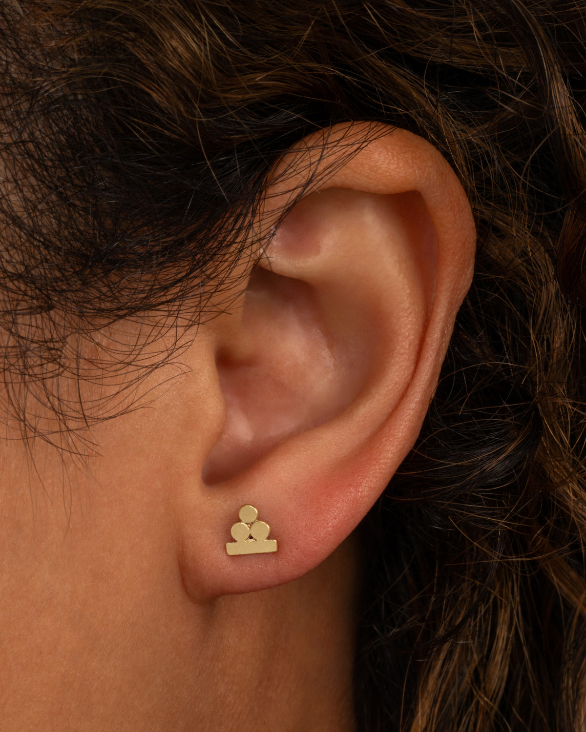 Lori Leven Balanced Circles stud earring in yellow gold worn on an ear, three brushed gold circles stacked on a flat base