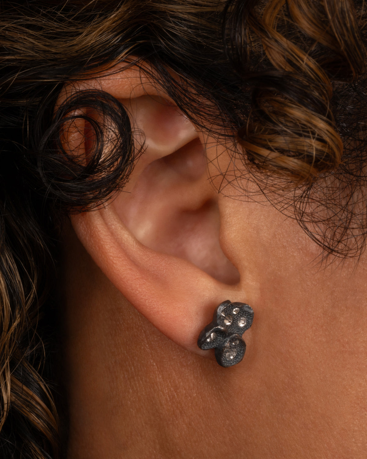 A pair of black oxidized stud earrings with inverted diamonds, shown on a person.