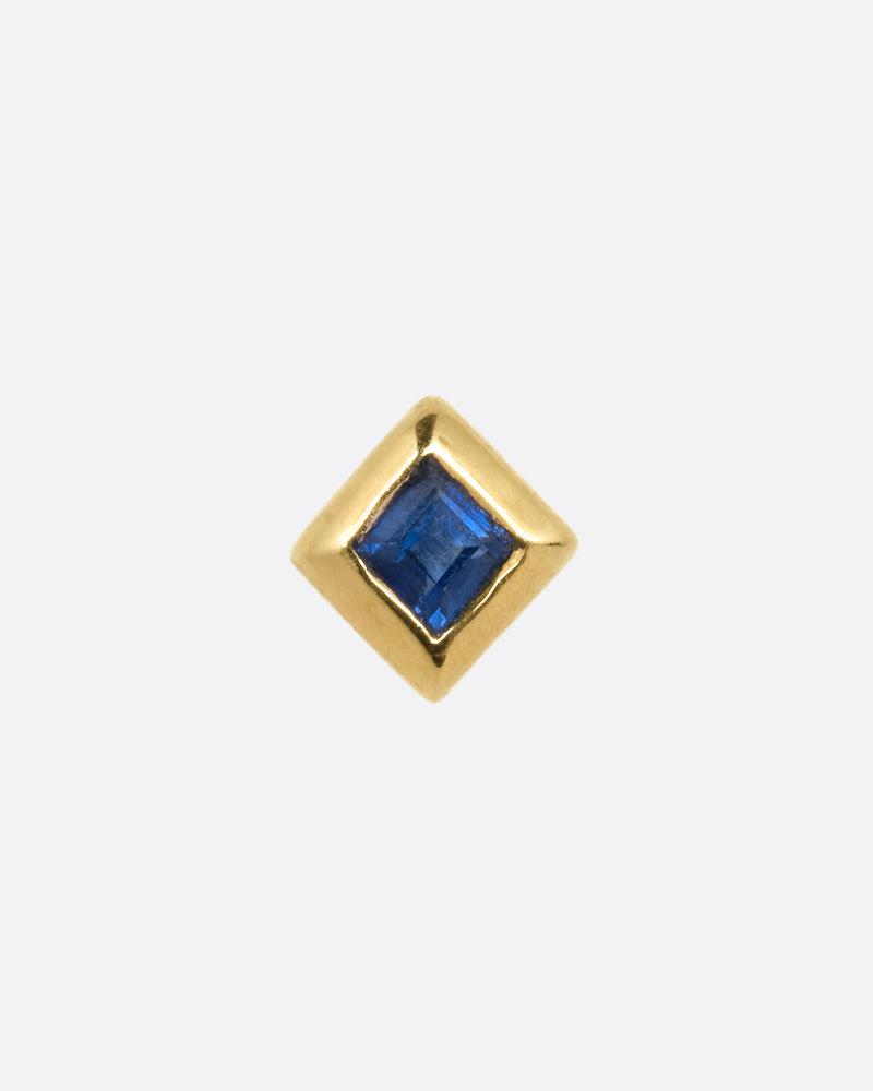 A yellow gold stud earring with a princess cut sapphire. Shown from the front.