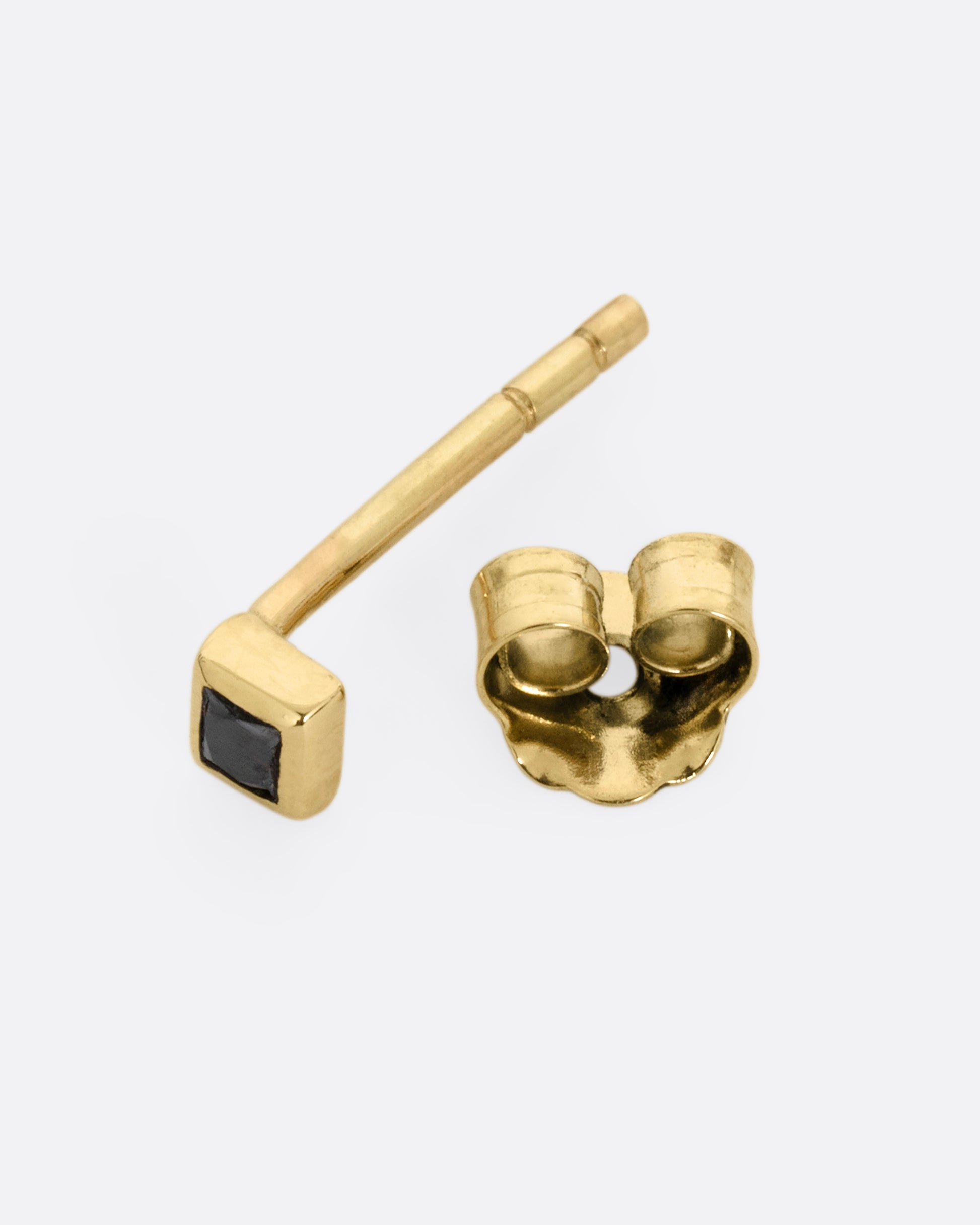 A yellow gold stud earring with a princess cut black diamond, shown open on it side.