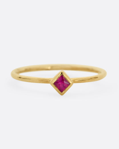A yellow gold ring with a princess cut ruby, shown from the front.