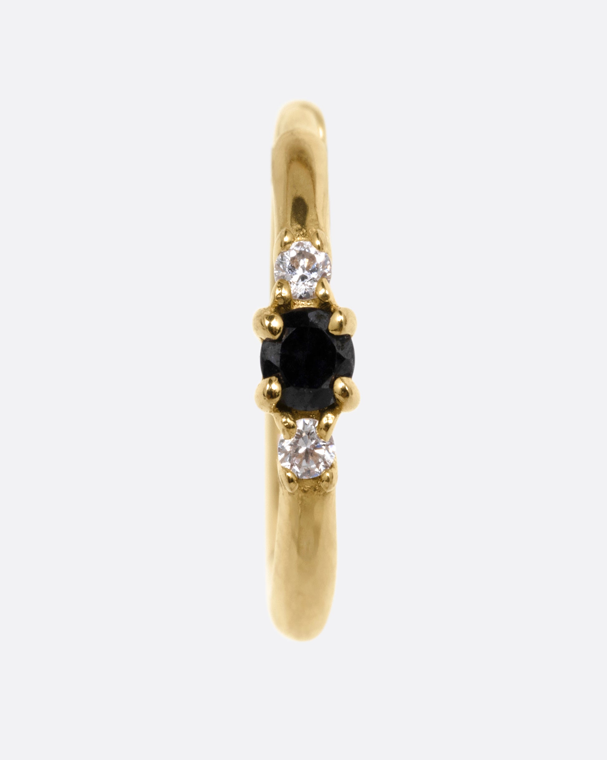 A yellow gold huggie hoop with two white diamonds and a black diamond, shown from the front.