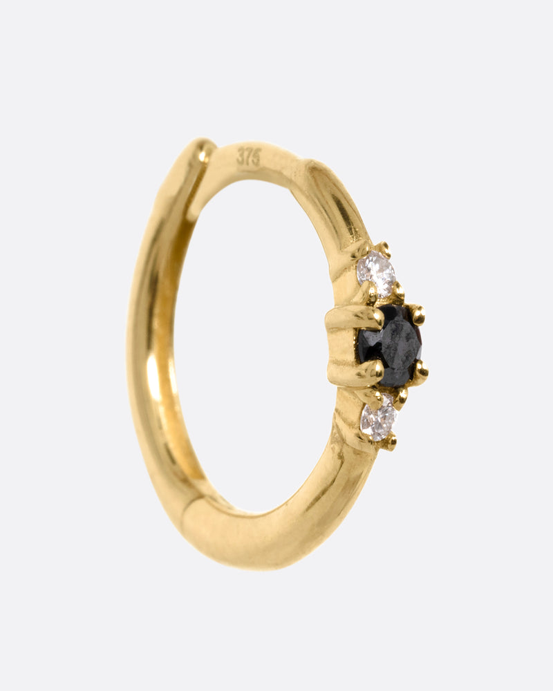 A yellow gold huggie hoop with two white diamonds and a black diamond, shown from the side.