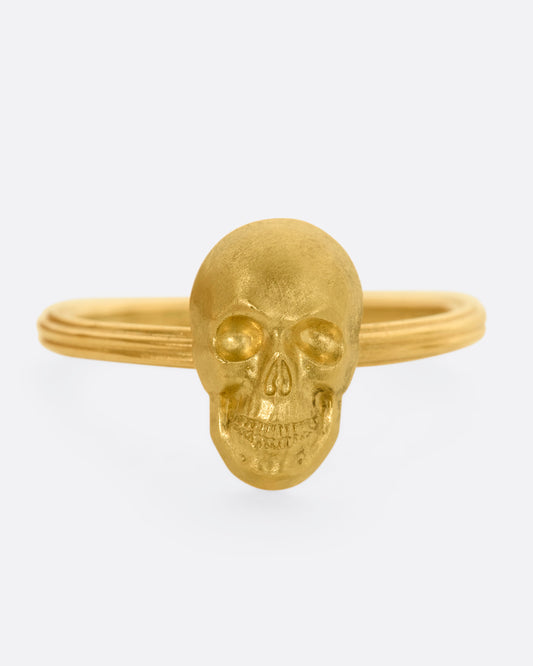 Front view of yellow gold ring with a sculpted skull charm on a round fluted band. 