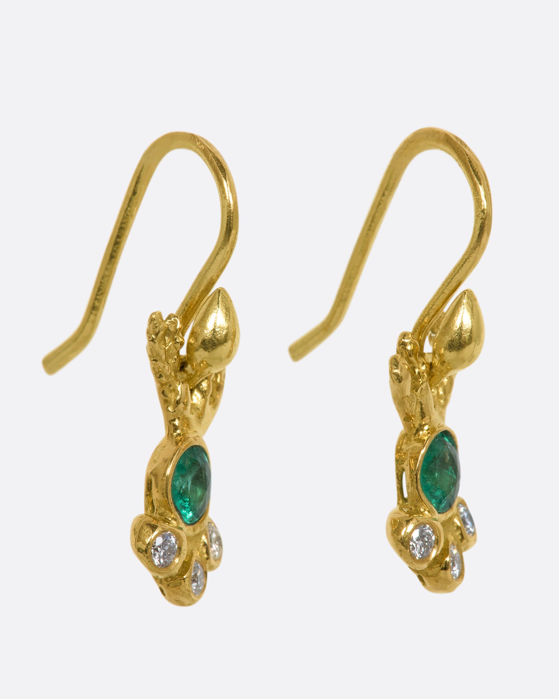 Yellow gold abstract ray earrings with an emerald at the center and three diamonds clustered below. View from the side.