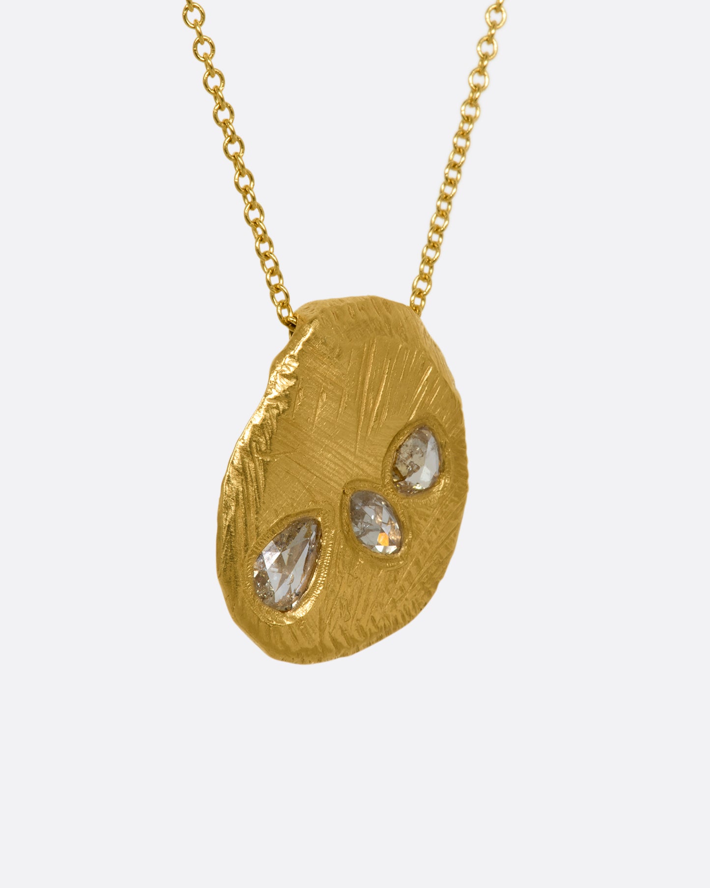 A heavy, hand carved, sliding gold pendant with three rose cut diamonds on a cable chain. View from the side.