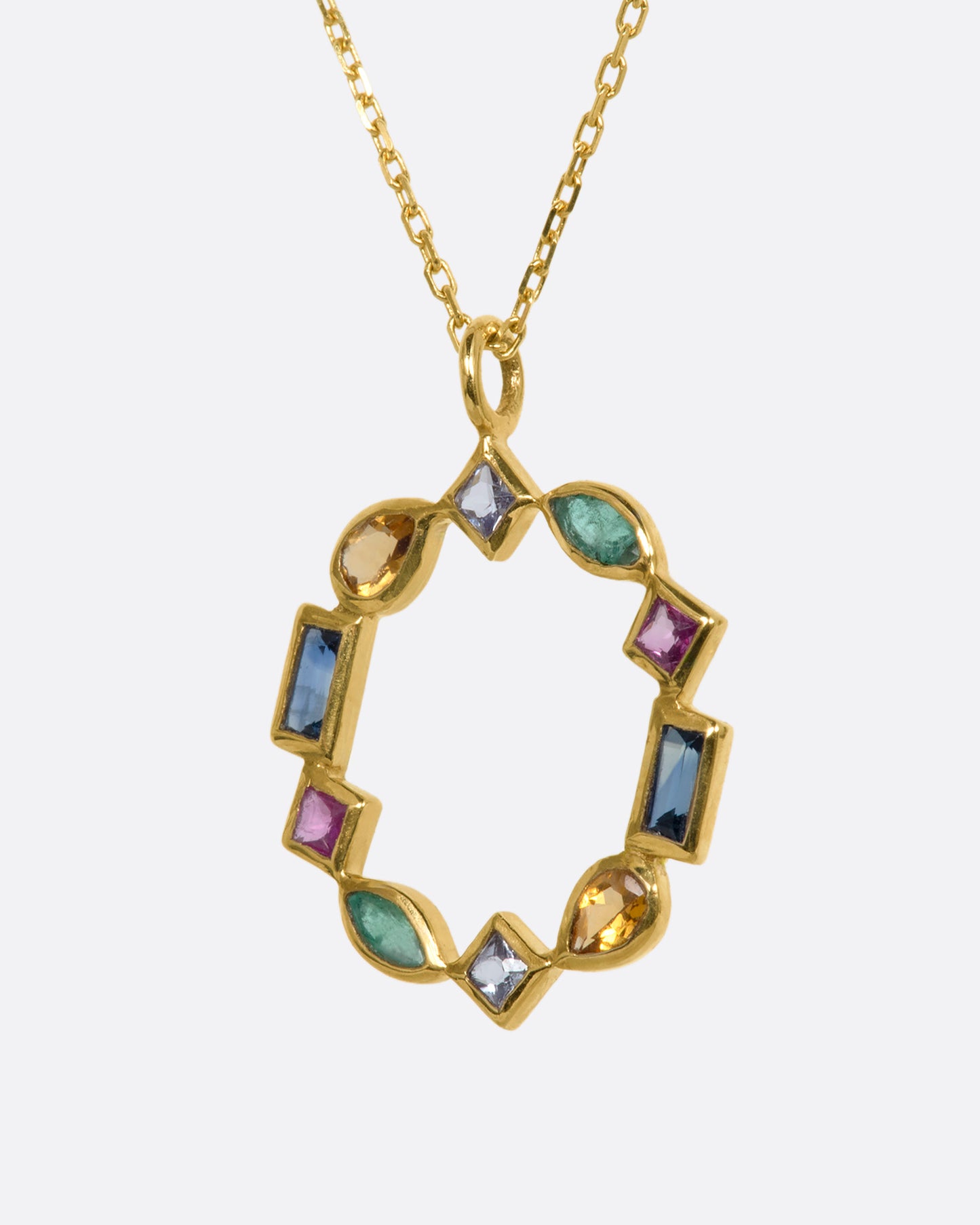 A circular yellow gold pendant made of emeralds, rubies, sapphires, tanzanite, and citrine. Shown from the side.